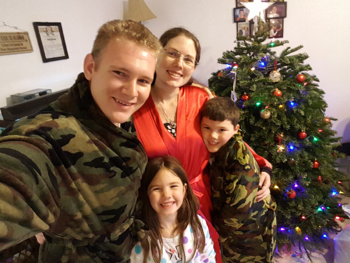 Sam smiling with his wife and kids beside their Christmas tree