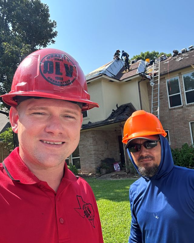 Sam The Roof Man in a red hard hat on a job site, with a crew working on the roof behind him