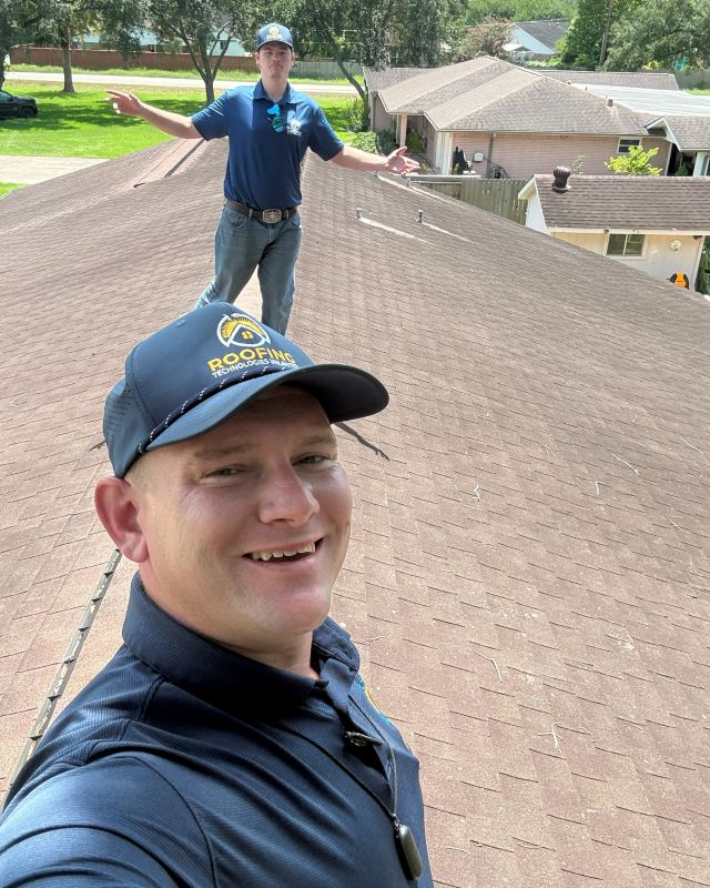Samuel Smith, Sam The Roof Man, smiling on a rooftop with a trainee standing on the ridge behind him