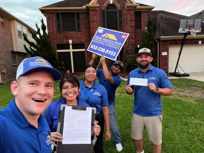 Sam and his team in front of a home, holding a signed contract and a yard sign